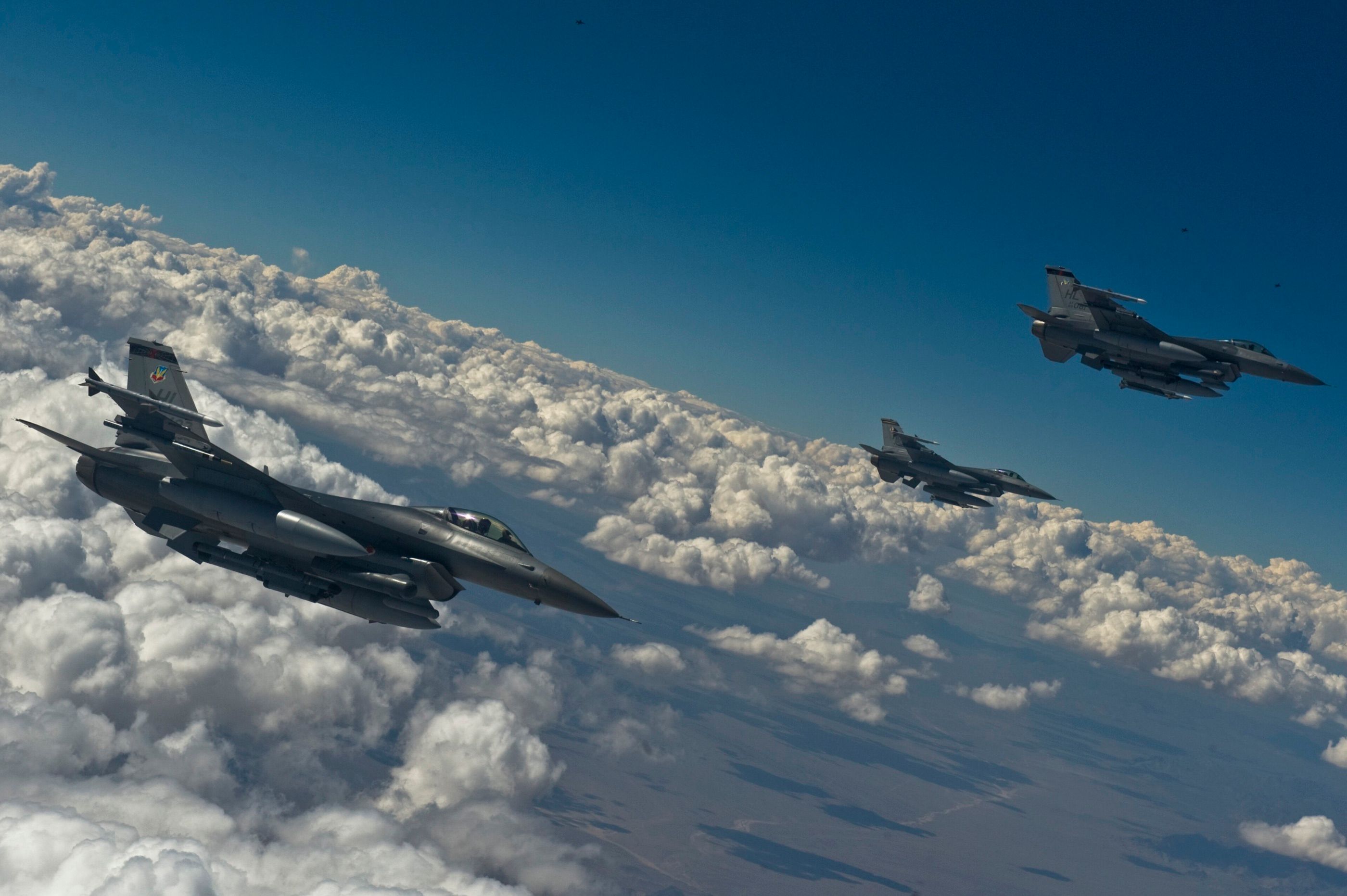 Three F-16s in formation above a sea of cumulus clouds during Red Flag